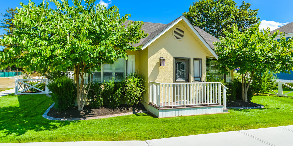 Charming small yellow home with a bright green lawn and landscaping